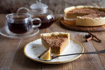A piece of pumpkin pie on a plate, a glass Cup of tea and a pumpkin pie on a wooden platter on an old wooden table