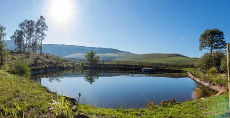 Smooth and Calm Dam With The Bright Sun, Blue Sky and Reflective Water, Panorama With A Floating Pontoon in Underberg South Africa