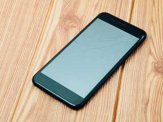 The broken smartphone display on wood background.