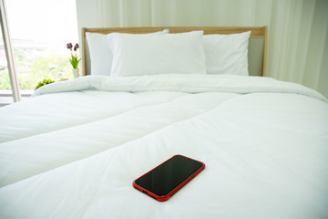 Modern smartphone in red color left on the bed in bedroom close up, photograph with copy space.