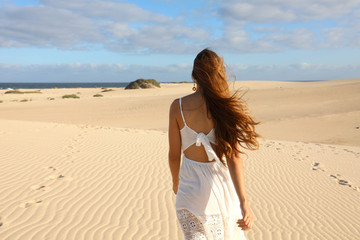Fototapeta na wymiar Amazing view of young woman walking barefoot on desert dunes at sunset in Corralejo, Fuerteventura
