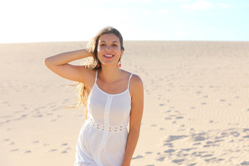 Fototapeta na wymiar Beautiful woman with white dress walking on Corralejo desert dunes looking at camera, Fuerteventura, Spain