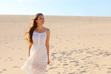 Fototapeta na wymiar Beautiful woman with white dress walking on dunes in desert, Corralejo, Fuerteventura, Spain