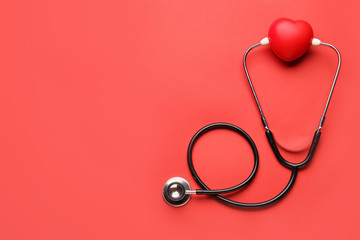 Stethoscope and heart on color background