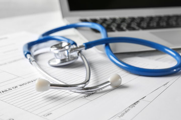 Modern stethoscope, laptop and documents on table