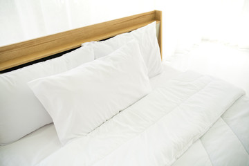 Fototapeta na wymiar Bedroom decorated in minimal style, photograph of white pillows and wooden bed in bedroom with natural light from window.