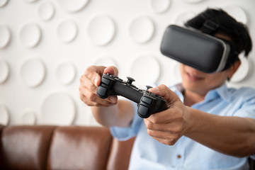 Asian adult man playing video game by using Virtual Reality goggle (VR) in the living room. Photograph with copy space.