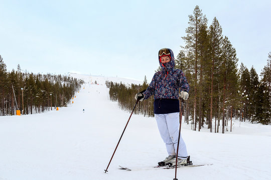 Female skier with skis smiling and wearing ski glasses. With reflection panorama of mountains. Ski resort Levi, Lapland, Finland
