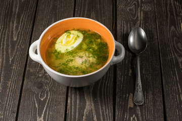 Soup with noodles, chicken, egg and dill on a dark wooden background in a plate with a spoon
