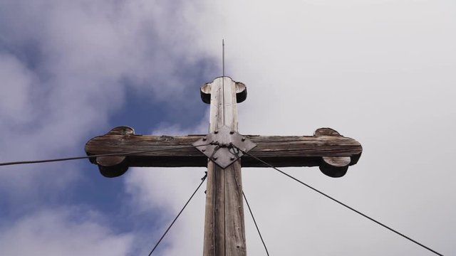 Tilt up towards the cross located on the peak of a mountain in Alpbach, as it shows the cludy sky as its background.