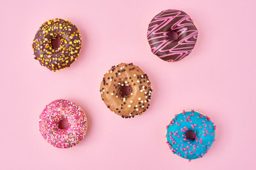 Different types of a colorful donats decorated sprinkles and icing on pastel pink background