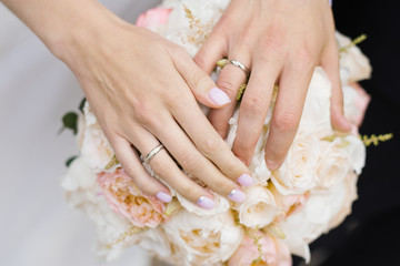 Obraz na płótnie Canvas Hands of the newlyweds, the bride and groom, with wedding rings on a wedding bouquet of white and milk roses and peonies close-up. Wedding couple