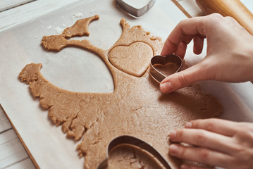 Making gingerbread cookies in the shape of a heart for Valentines Day. Woman hand use cookie cutter. Holiday food concept