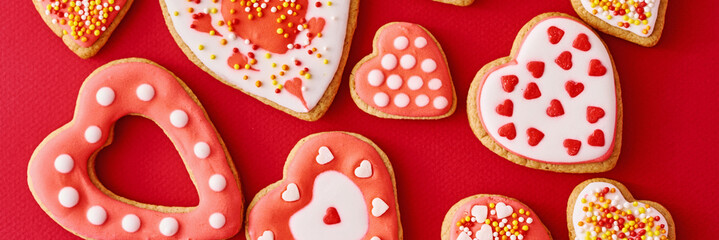 Background of decorated with icing and glazed heart shape cookies on the red background, long banner. Valentines Day food concept