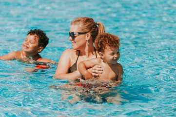 Fototapeta na wymiar Happy young mother playing with kids in pool on a hot summer day