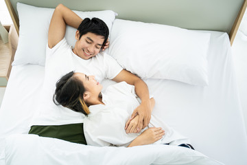 Asian husband and wife relaxing on the bed together in the morning.