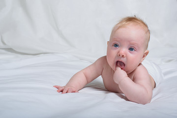 Cute baby on his stomach. He looks up and holds a finger in his mouth. White background
