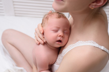 Mother with a blond sleeping baby in her arms, a moment of tenderness. Close-up