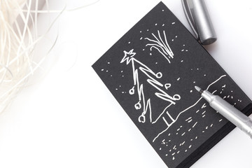 White pen and black notebook. Painting tools on a black background. Images of notebook page with black paper. Christmas tree and ball . Winter holiday greeting layout