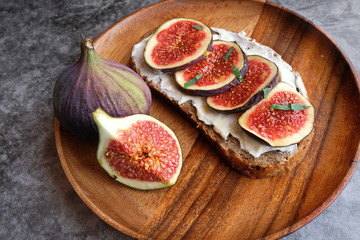 Rye and spelt sourdough toast with creamy yogurt and feta cheese, fresh figs with honey, next to pieces of fresh figs with cinnamon on a large wooden plate.