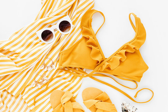 Yellow dress with stripes with slippers, sunglass and cute swimsuit. Women's stylish summer outfit. Trendy clothes. Flat lay, top view.