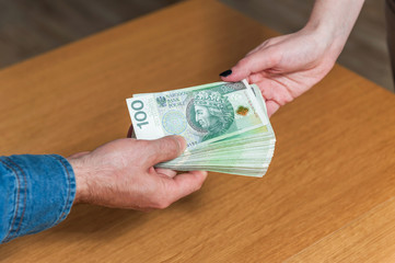 Close up of man hand giving pile of Polish money to woman hand. Wooden table background. Polish money banknotes