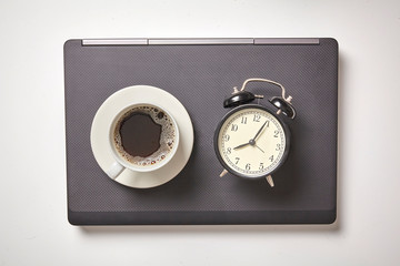 Naklejka premium Flat lay on workspace with laptop computer, alarm clock and black coffee. White background, top view.