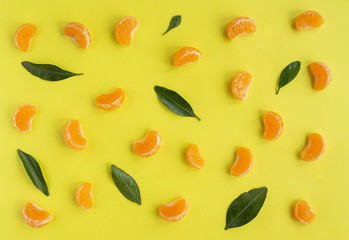 Flat lay with orange tangerines, mandarin slices, leaves on yellow background.  Top view, copy space.  