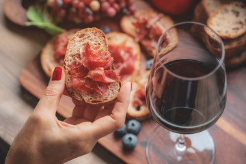 Selective foucs on finger holding ham jamon serrano and glasses of red wine  on wooden board