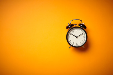 Black alarm clock on yellow background. Close up. Top view.