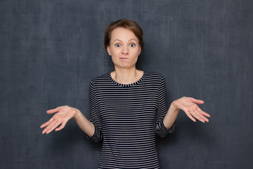 Portrait of confused young woman raising hands and shrugging shoulders
