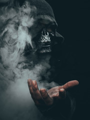 Uomo con maschera di teschio che tende la mano in mezzo al fumo