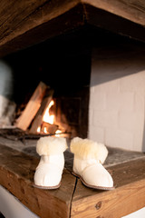 Fototapeta na wymiar White lamb wool slippers houseshoes next to fireplace. Keep your feet warm and cozy during the freezing cold season
