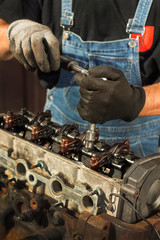 Mechanik samochodowy w warsztacie rozkręca kluczem nasadowym element silnika samochodu osobowego. 