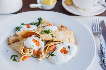 White plate with pancakes with salmon and red caviar, served with sour cream for breakfast