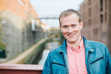 Handsome smiling caucasian man, stylishly dressed head and shoulders portrait looking confident at the camera standing on a bridge over a canal in Georgetown, Washington DC.  - 312826310