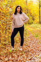 Young girl with beige sweater and black jeans stands in the colorful autumn forest in October in Bavaria, Germany