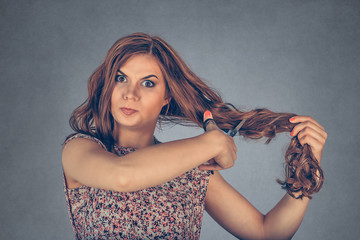Frustrated woman holding her hair and scissors about to cut her hair - obrazy, fototapety, plakaty