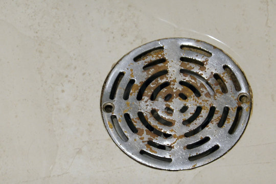 Old rusty round shower drain strainer in bathroom floor.