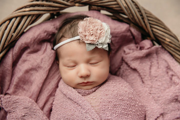 sweet newborn baby girl swaddled and bundled up in a blanket wrap laying in a wooden basket close up