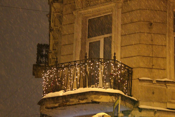 balcony of an old building decorated with a garland on a winter evening during a blizzard
