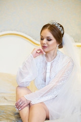 The bride in a white coat on the bed in a wedding morning