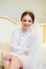 The bride in a white coat on the bed in a wedding morning