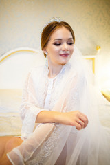 The bride in a white coat on the bed in a wedding morning