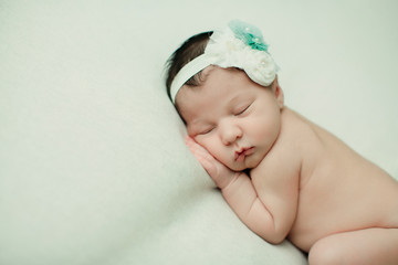 Sweet newborn infant baby girl laying on a cream colored neutral background