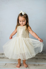 pretty preschool-age girl wearing a gold and white sequined dress and a white bow spinning and...