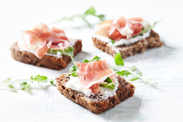 Tasty sandwiches with cream cheese, smoked ham and fresh herbs. Bright wooden background. Close up.