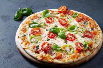 Pizza with mozzarella cheese. cherry tomatoes, jalapeno pepper, capers and fresh basil on dark stone background. 
