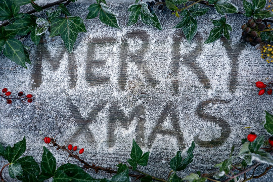 Weihnachtshintergrund Merry Christmas mit Handlettering, Holz, wei&szlig;er Schnee, feierliche Dekoration, rote Beeren, gr&uuml;ner Efeu, Stechpalme