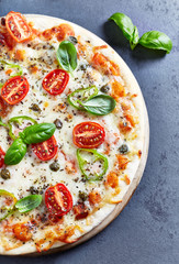 Pizza with mozzarella cheese. cherry tomatoes, jalapeno pepper, capers and fresh basil on dark stone background.
